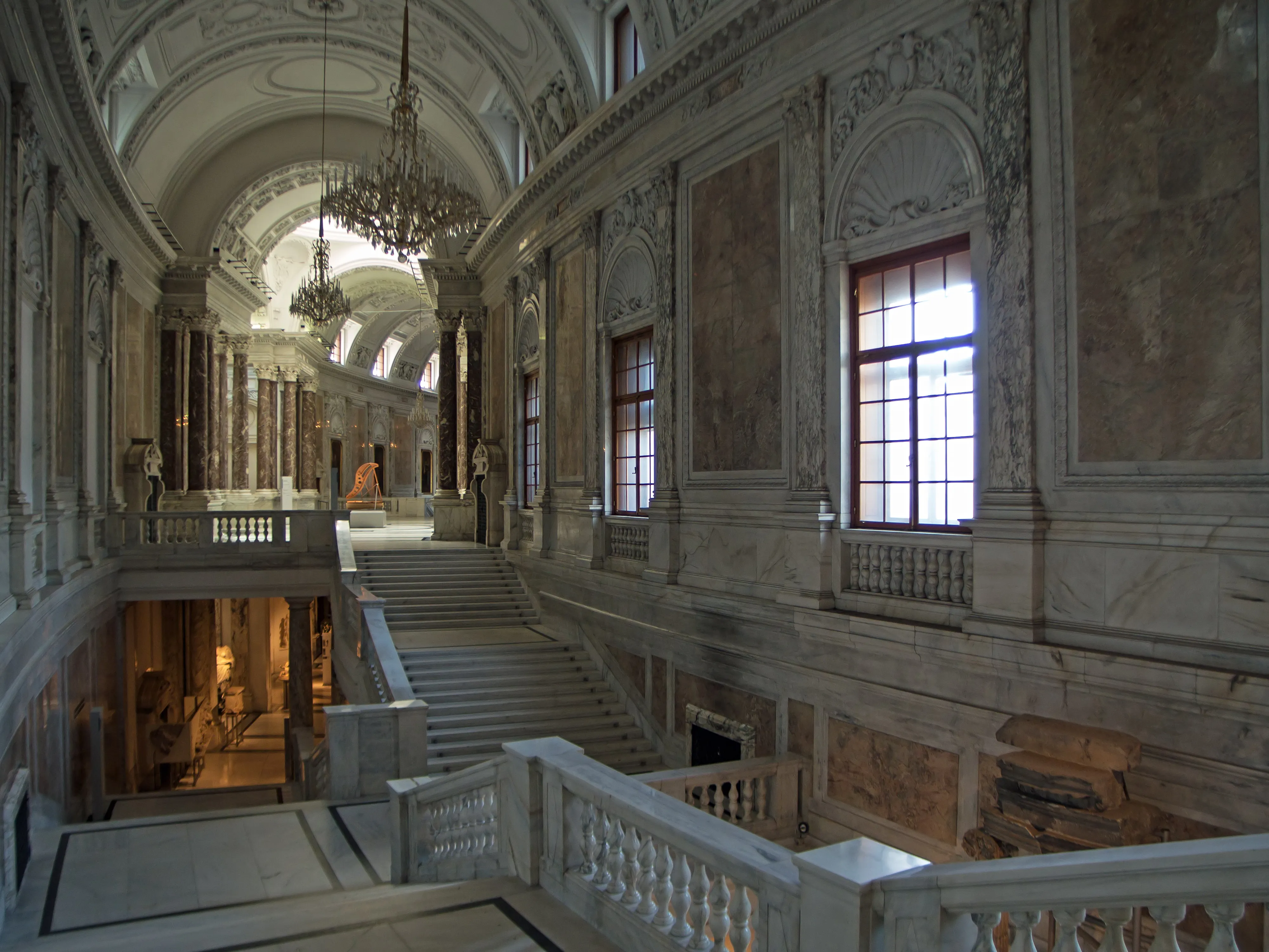 Interior of a grand hall with marble staircase, chandeliers, and ornate architectural details