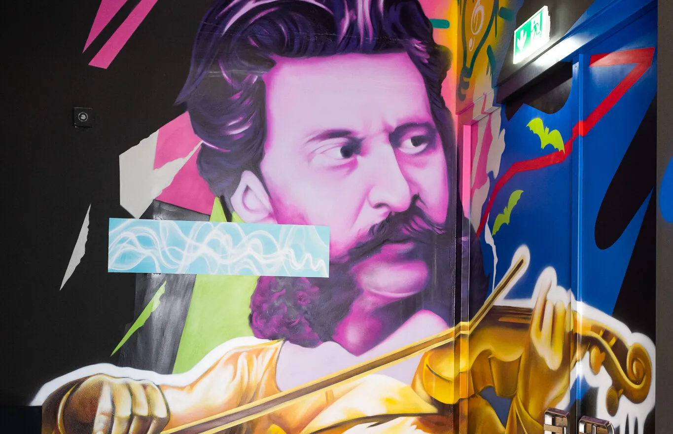 Un colorido mural que representa a un hombre con bigote tocando el violín, rodeado de formas y patrones abstractos.