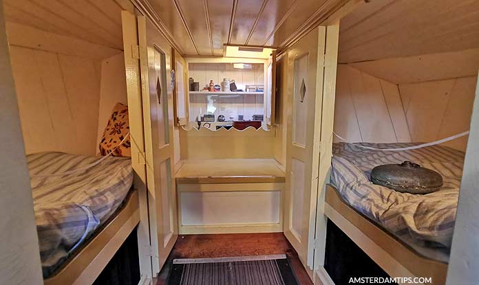 Gezellig houten interieur van een grachten houseboat met twee bedden, een kleine kitchenette en planken met huishoudelijke artikelen