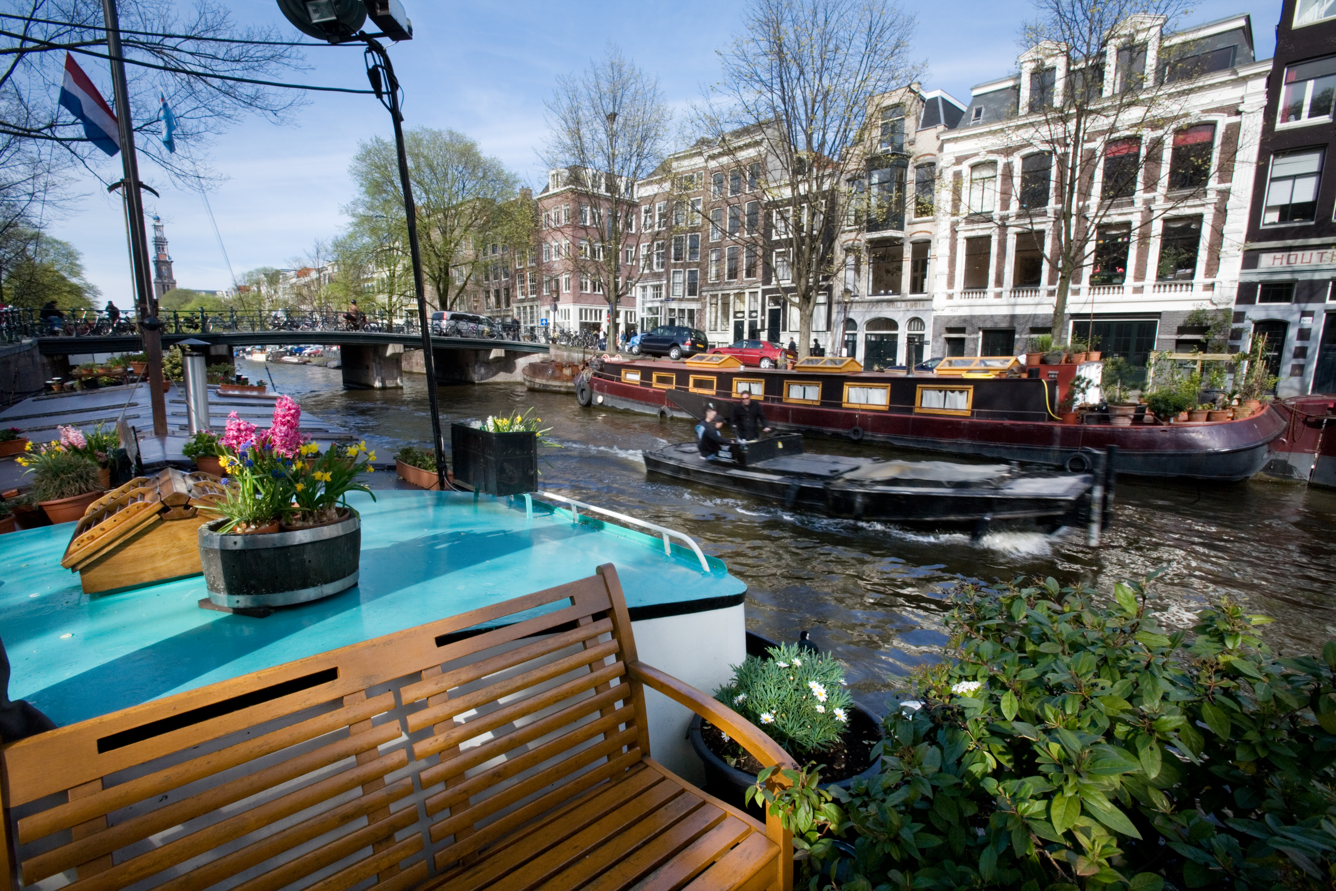 Canal scene with houseboats, historic buildings, wooden bench, and potted flowers along a waterway in Amsterdam