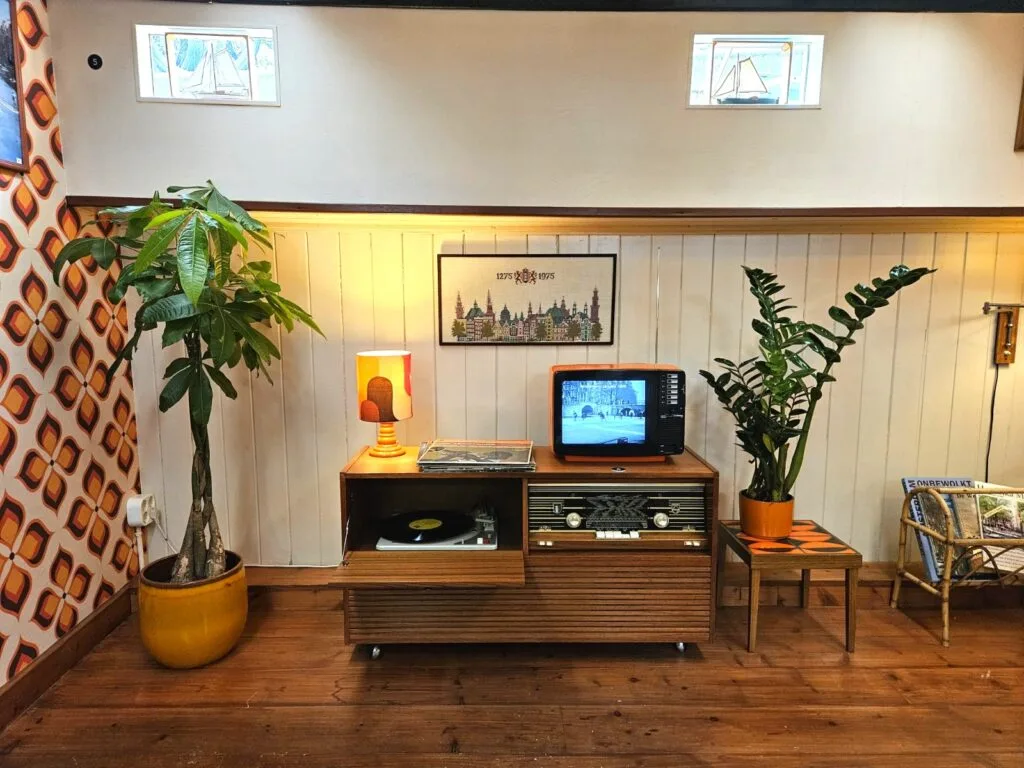 Houten interieur van een woonbootmuseum met vintage entertainmentcentrum, potplanten en wanddecoraties die het leven op de Amsterdamse grachten tonen