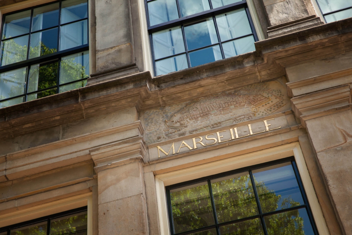 Stone facade of Huis Marseille Museum for Photography with 'MARSEILLE' engraved above a window and surrounding multi-paned windows