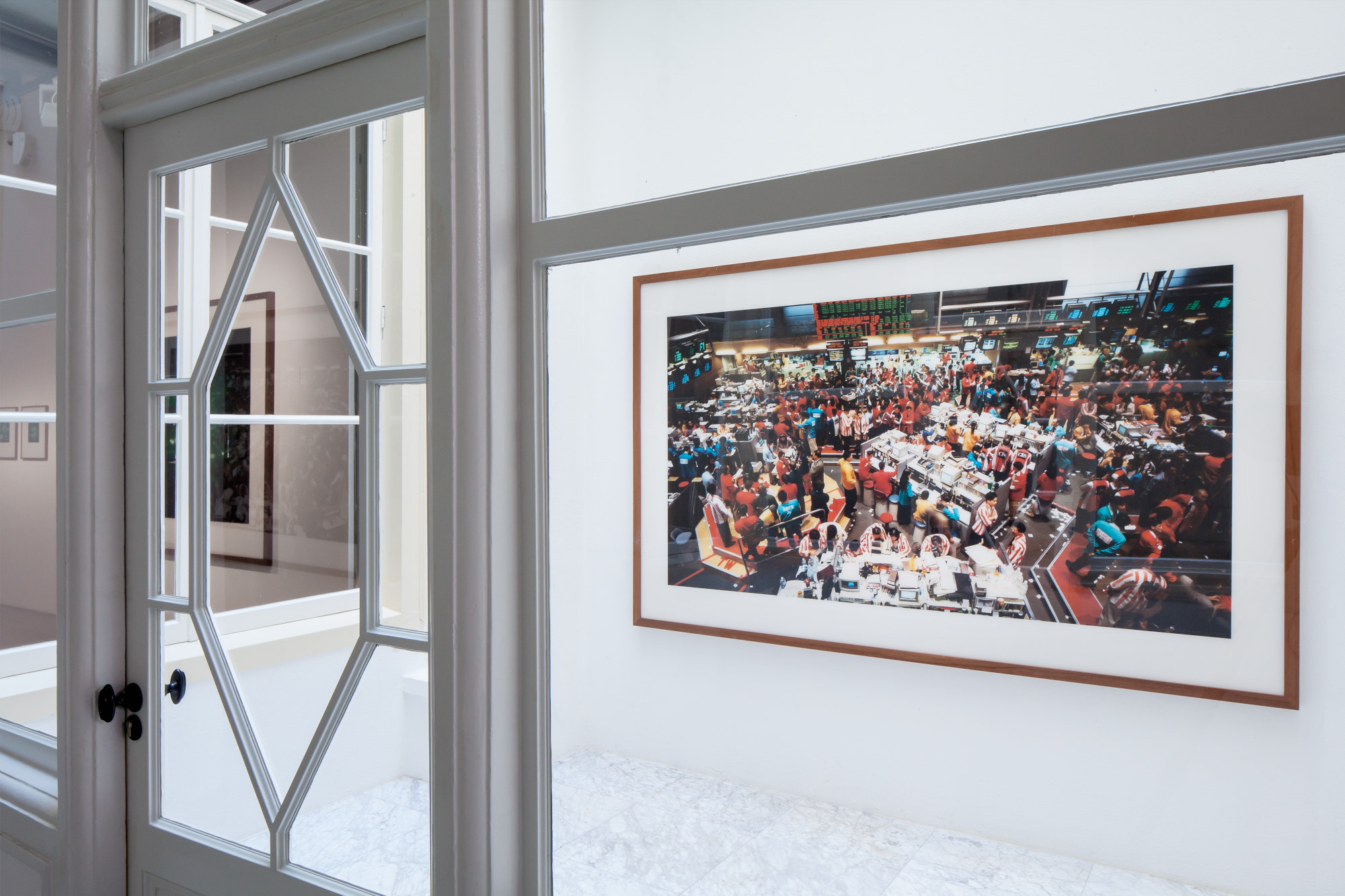 Framed color photograph on white wall showing crowded event with people at tables, viewed through glass-paneled door