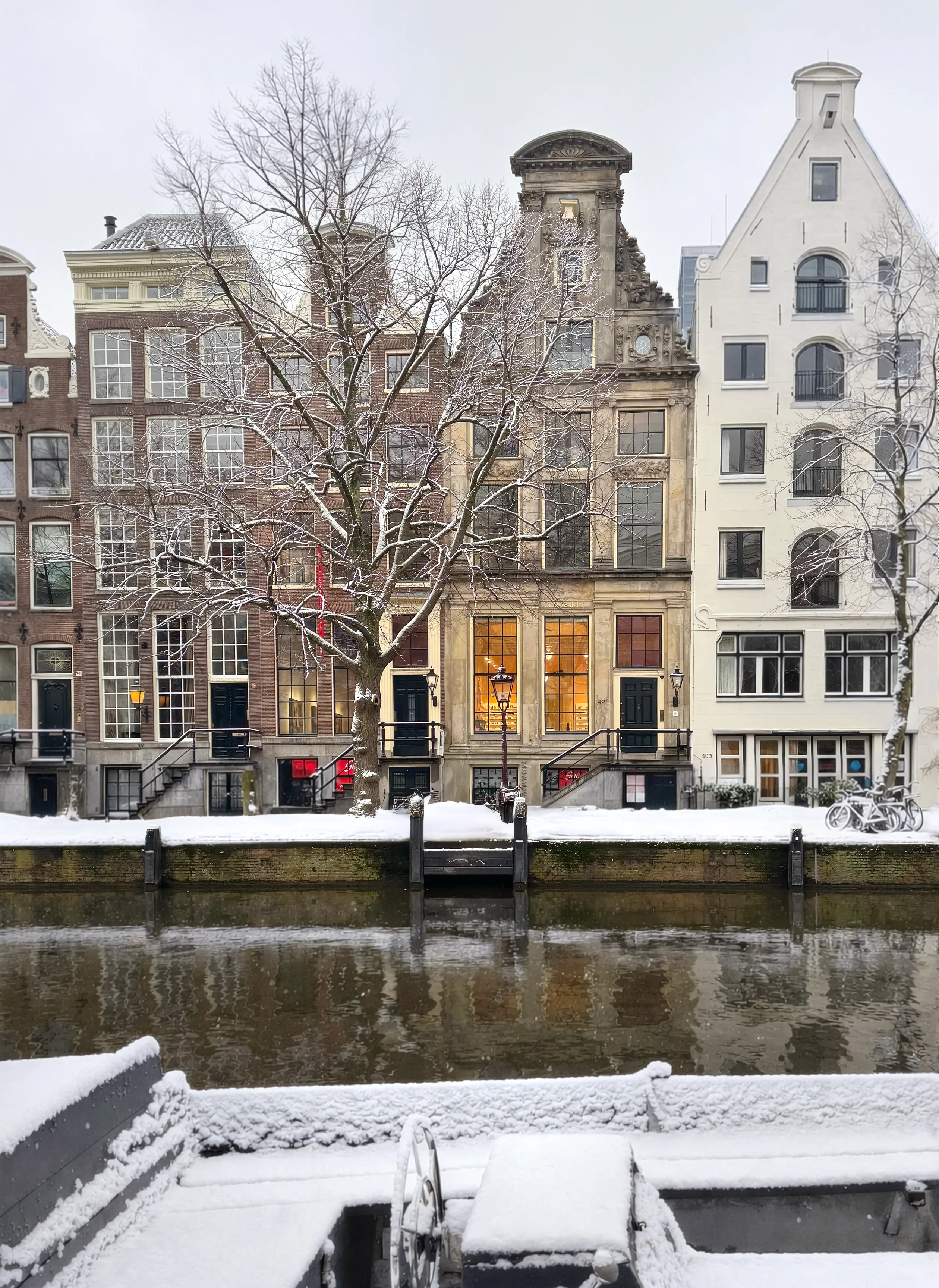 Snow-covered canal houses along a waterway, with a historic building featuring illuminated windows.