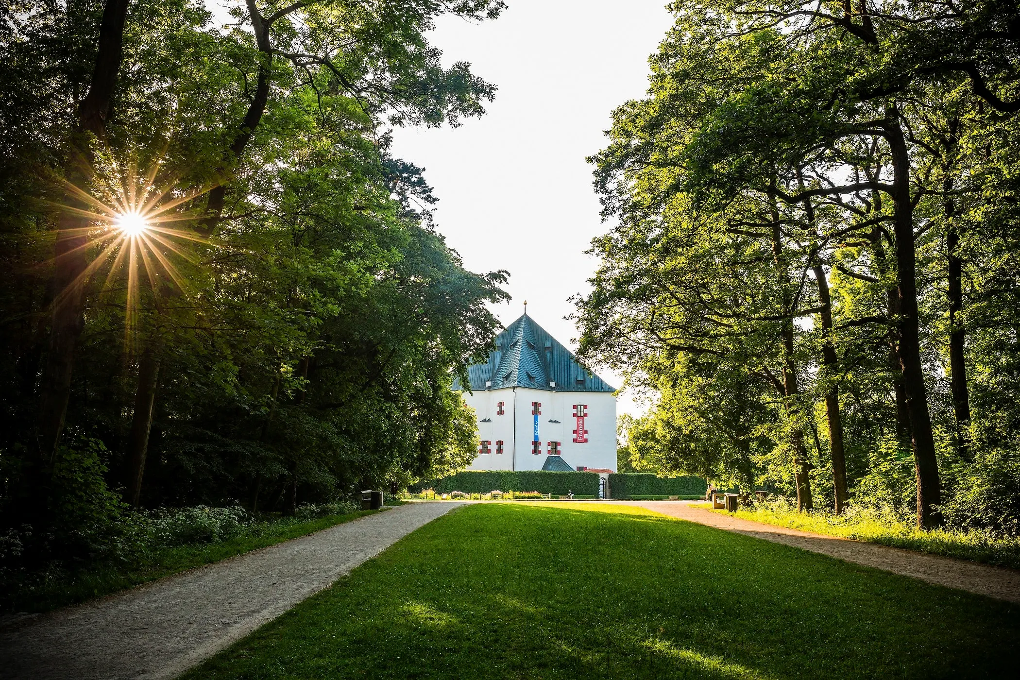 Stervormig wit gebouw met groen dak, omgeven door bomen en een graspad