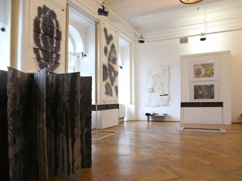 Interieur van een galerie met houten vloeren en witte muren waarop abstracte kunstinstallaties en schilderijen worden tentoongesteld