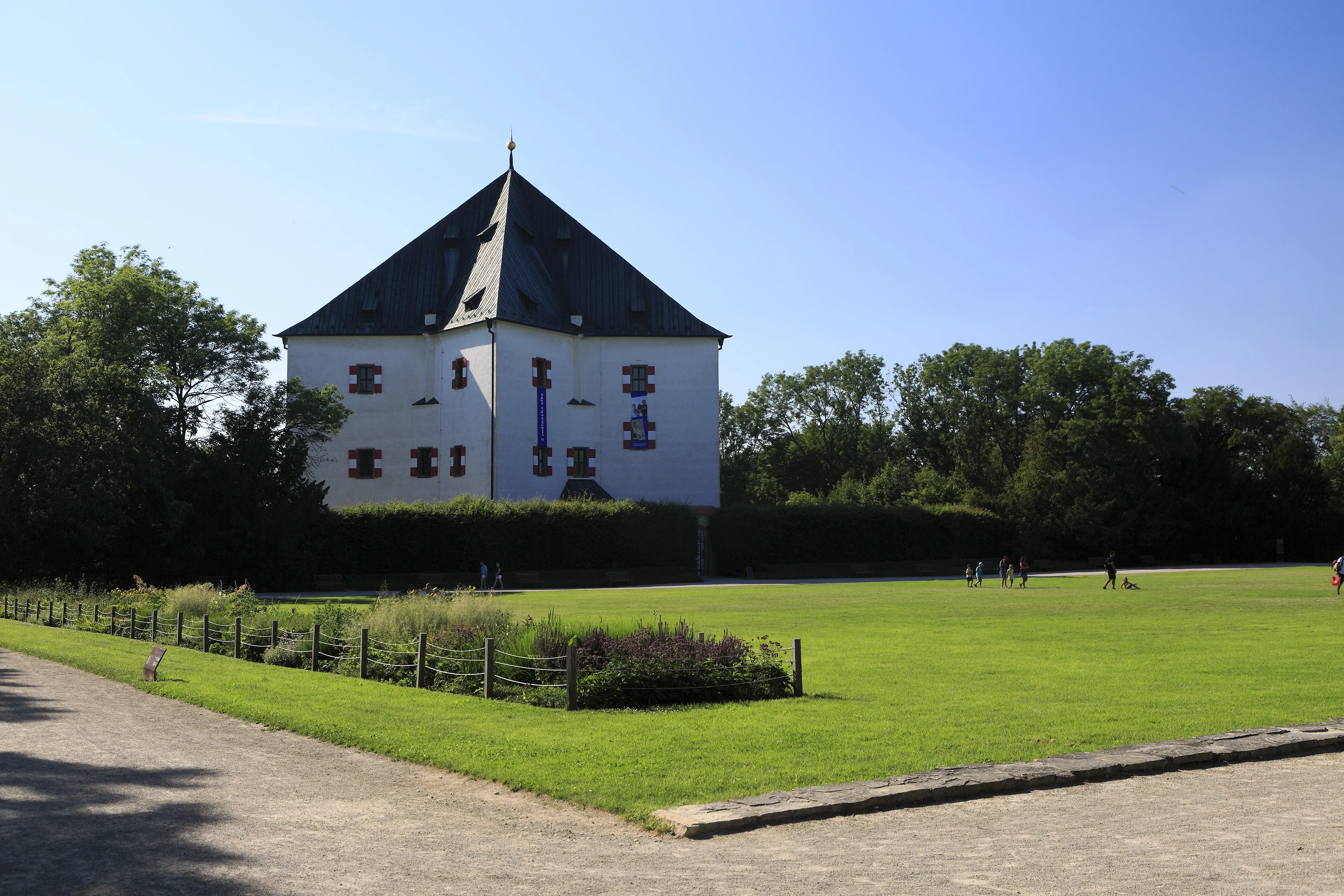 Stervormig wit gebouw met een donker dak, omgeven door groene grasvelden en bomen