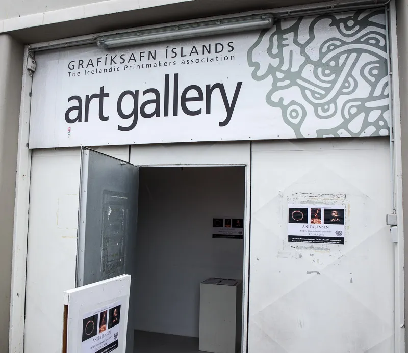 Biała fasada sklepu z dużym szyldem z napisem 'Grafíksafn Íslands The Icelandic Printmakers association art gallery' nad otwartymi drzwiami.