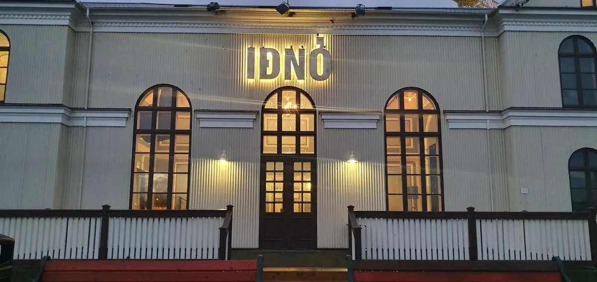 The illuminated IÐNÓ sign above the arched entrance of a white historic building at dusk