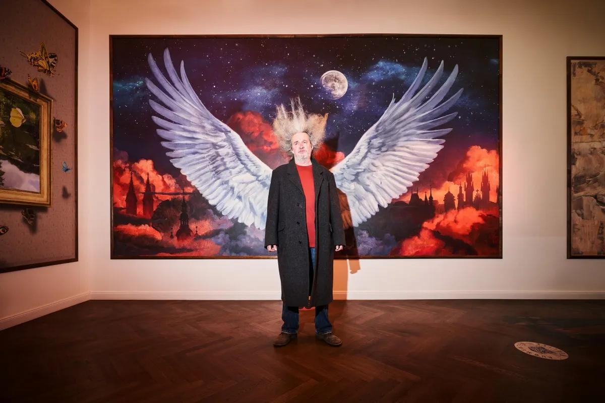 Een persoon die voor een groot schilderij van engelenvleugels met een maan en kleurrijke hemel staat in een museumgalerij