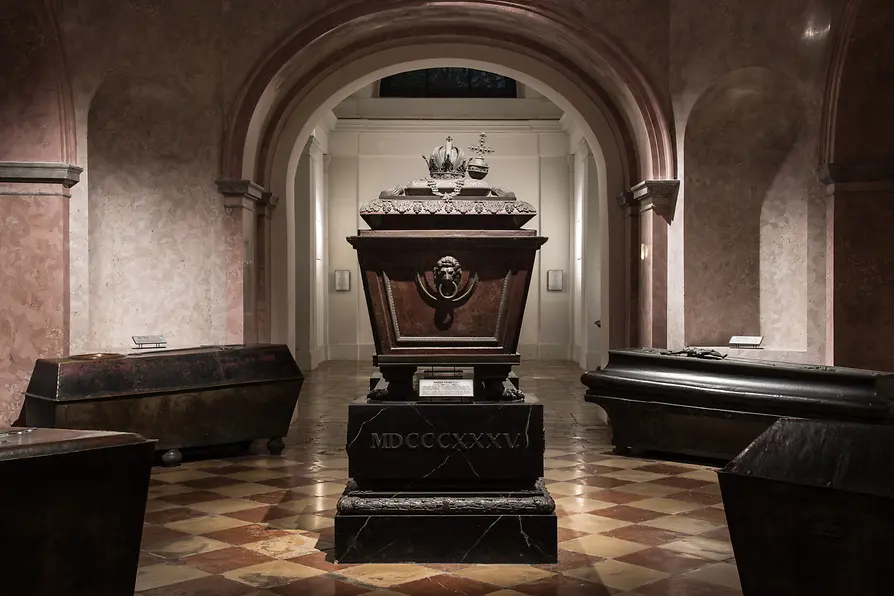 Sierlijke, donkere sarcofaag in het midden van een gewelfde kamer met boogdoorgangen en een betegelde vloer