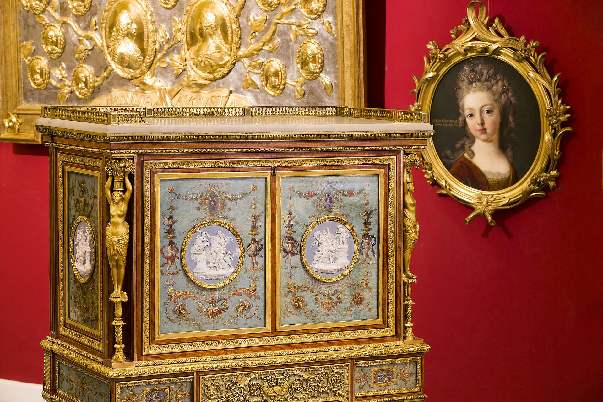 Armario ornamentado con detalles en azul y dorado y un retrato dorado sobre una pared roja