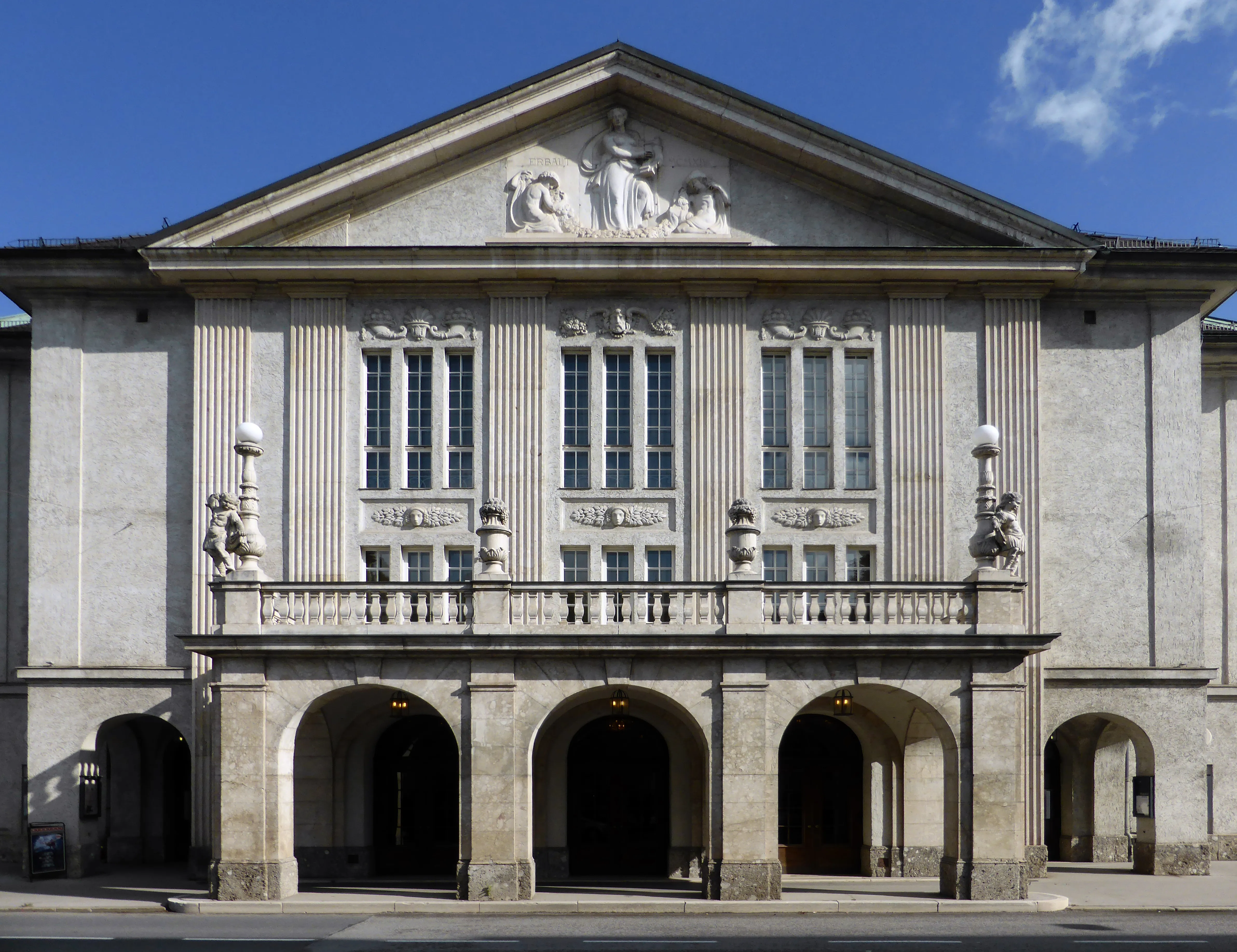 Neoclassical facade of the Mozarteum building in Salzburg featuring a triangular pediment with sculptures, arched entrance portico, and ornate stone balcony