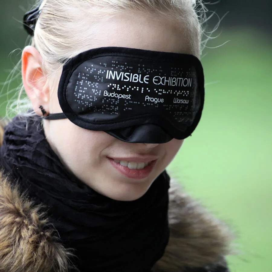 close-up van een persoon met een zwarte blinddoek met de tekst 'invisible exhibition' en braille