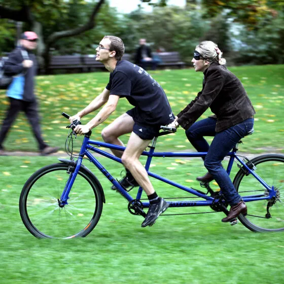 Twee mensen op een blauwe tandemfiets in een grasveld in een park