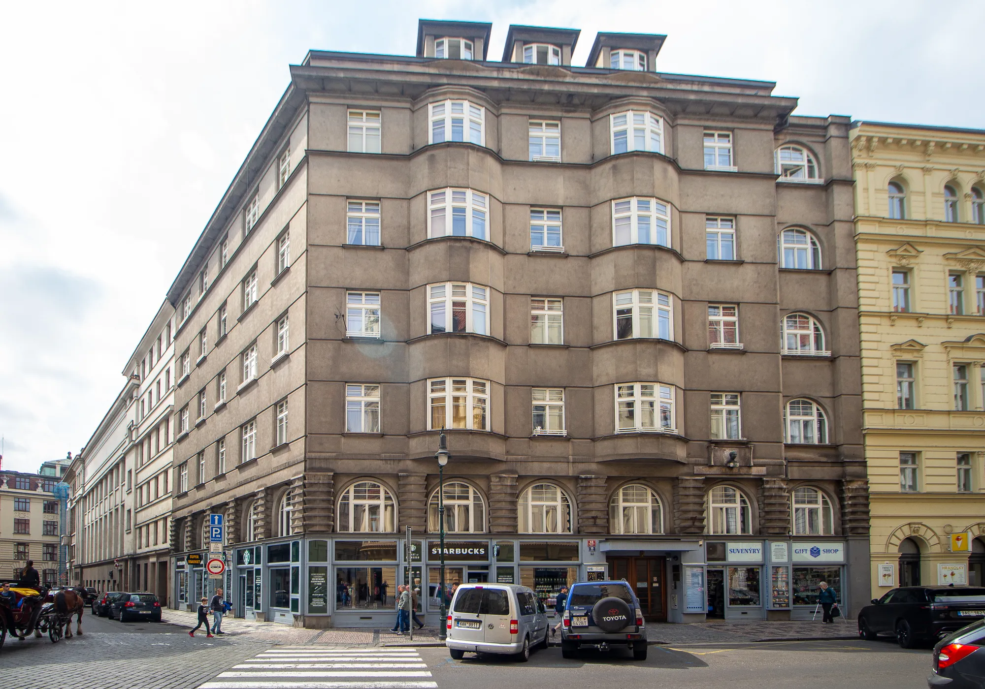 Wielopiętrowy brązowy budynek z łukowymi oknami i zakrzywioną fasadą przy ulicy miejskiej