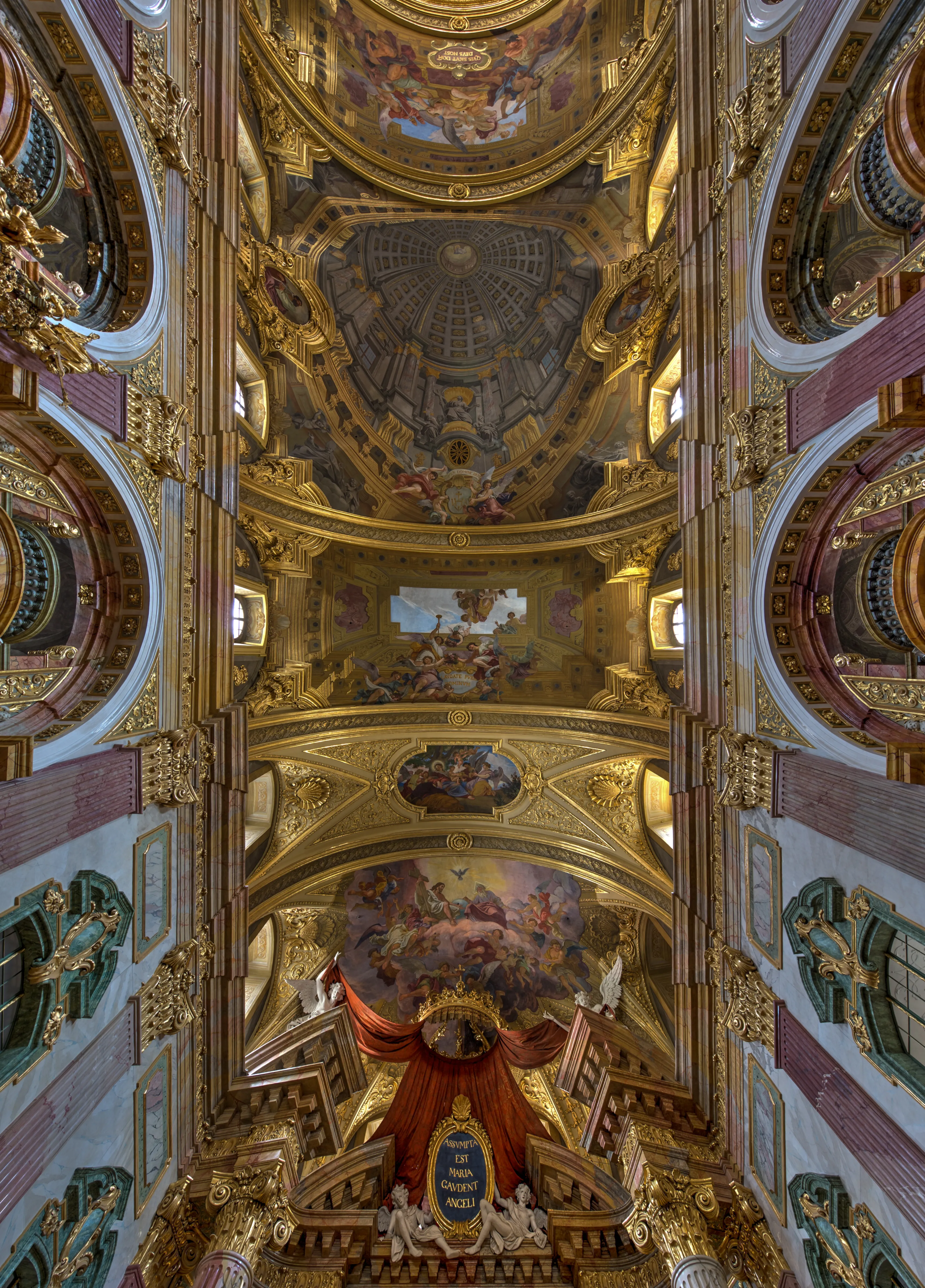 Vista interior de la Iglesia de los Jesuitas con un techo grandioso y ornamentado que presenta detalles dorados, frescos y una cúpula central.