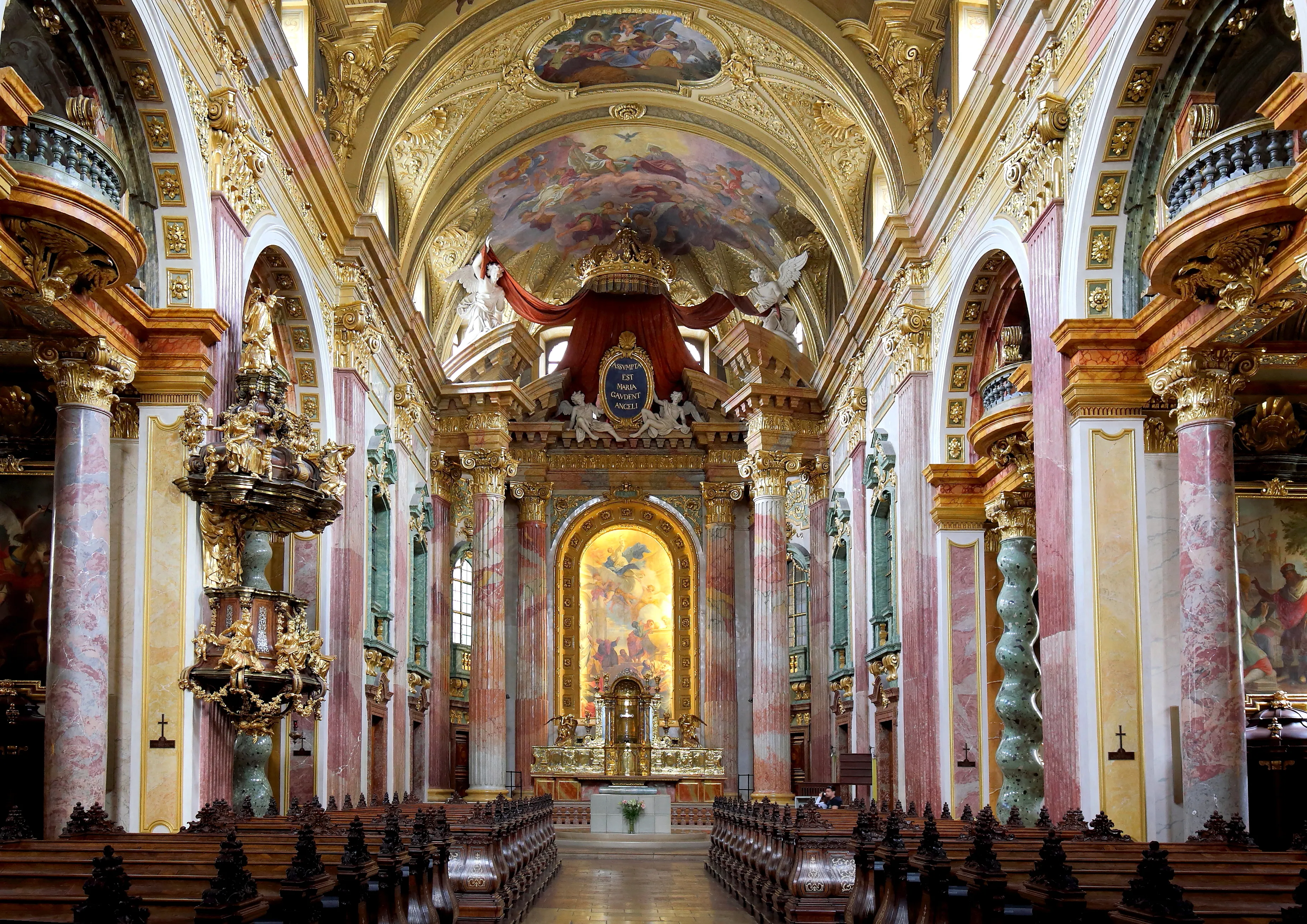 Sierlijk interieur van de Jezuïetenkerk met vergulde details, roze en witte zuilen, en een groot plafondfresco