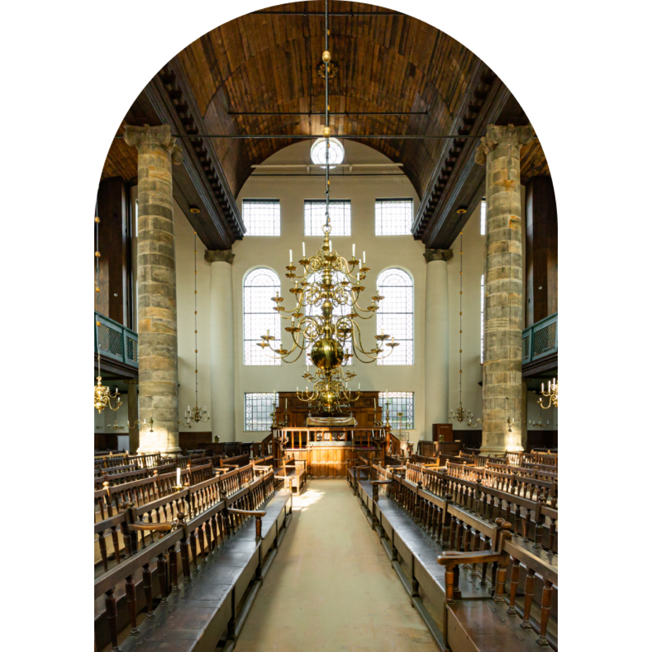 Przestronne wnętrze zabytkowej synagogi z drewnianymi ławkami, dużym żyrandolem, wysokimi oknami z łukami i kamiennymi kolumnami pod sklepionym drewnianym sufitem