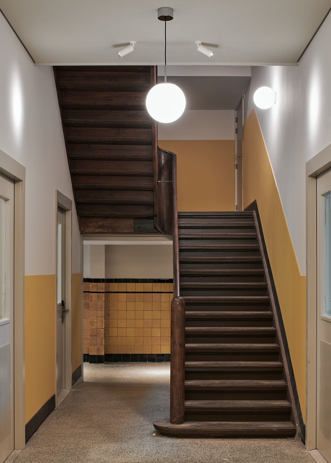 Interior hallway with wooden staircase, yellow and white walls, and modern round ceiling lights in a cultural venue
