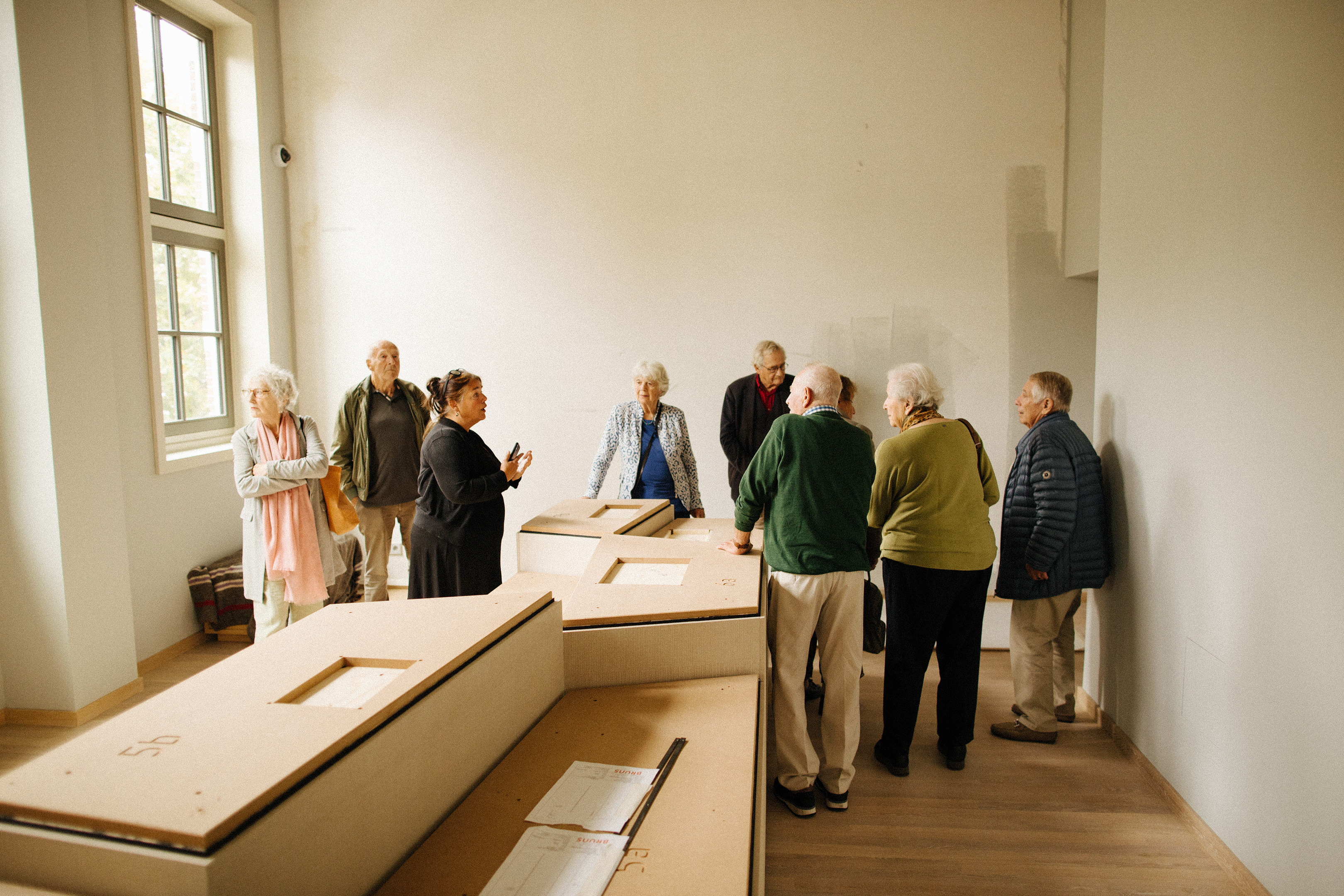 Group of visitors viewing exhibits in a bright, minimalist exhibition room with white walls and wooden flooring