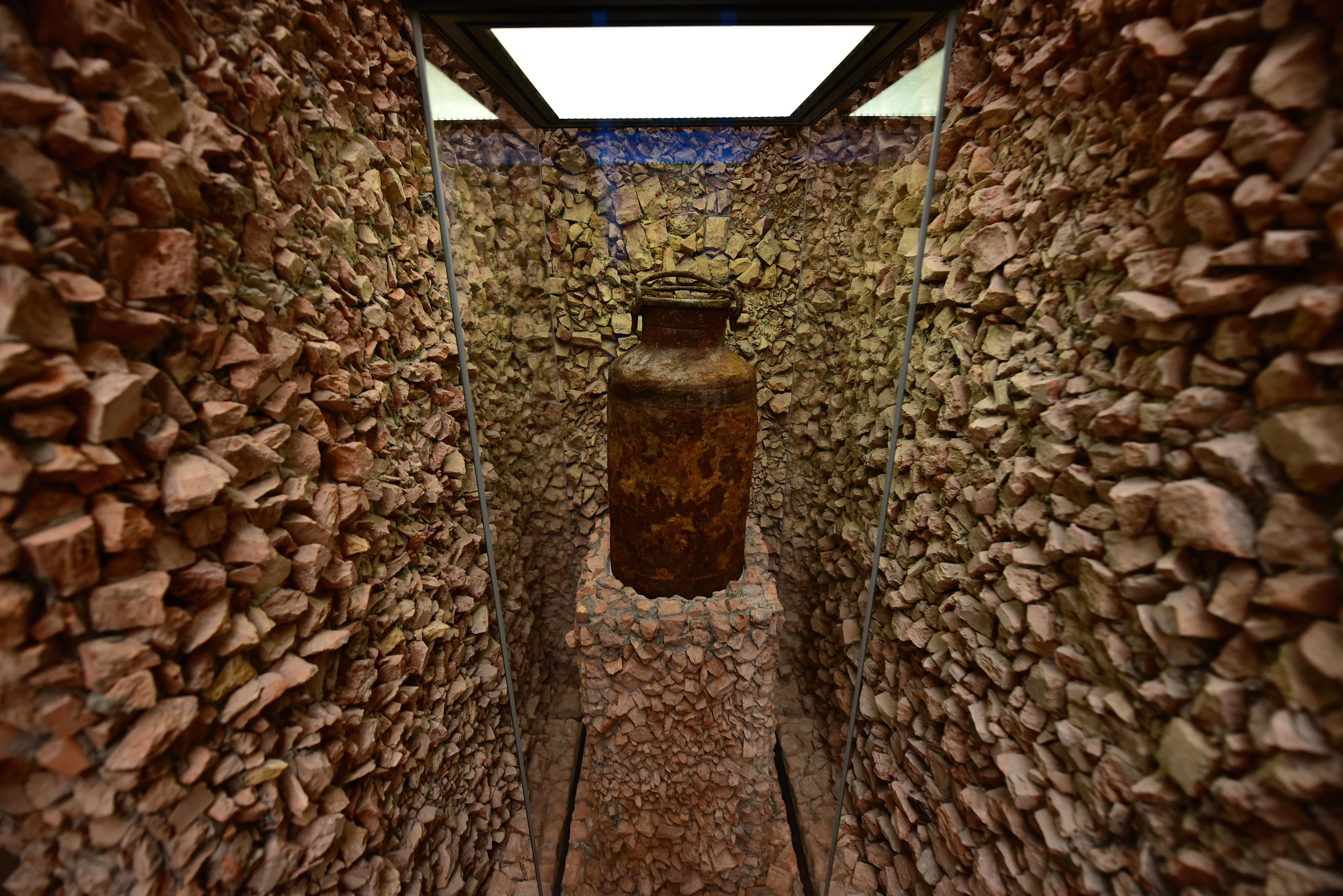 A rusted metal container in a narrow corridor with stone walls and a glass enclosure