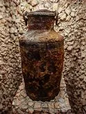 weathered metal container with lid on stone pedestal against textured wall
