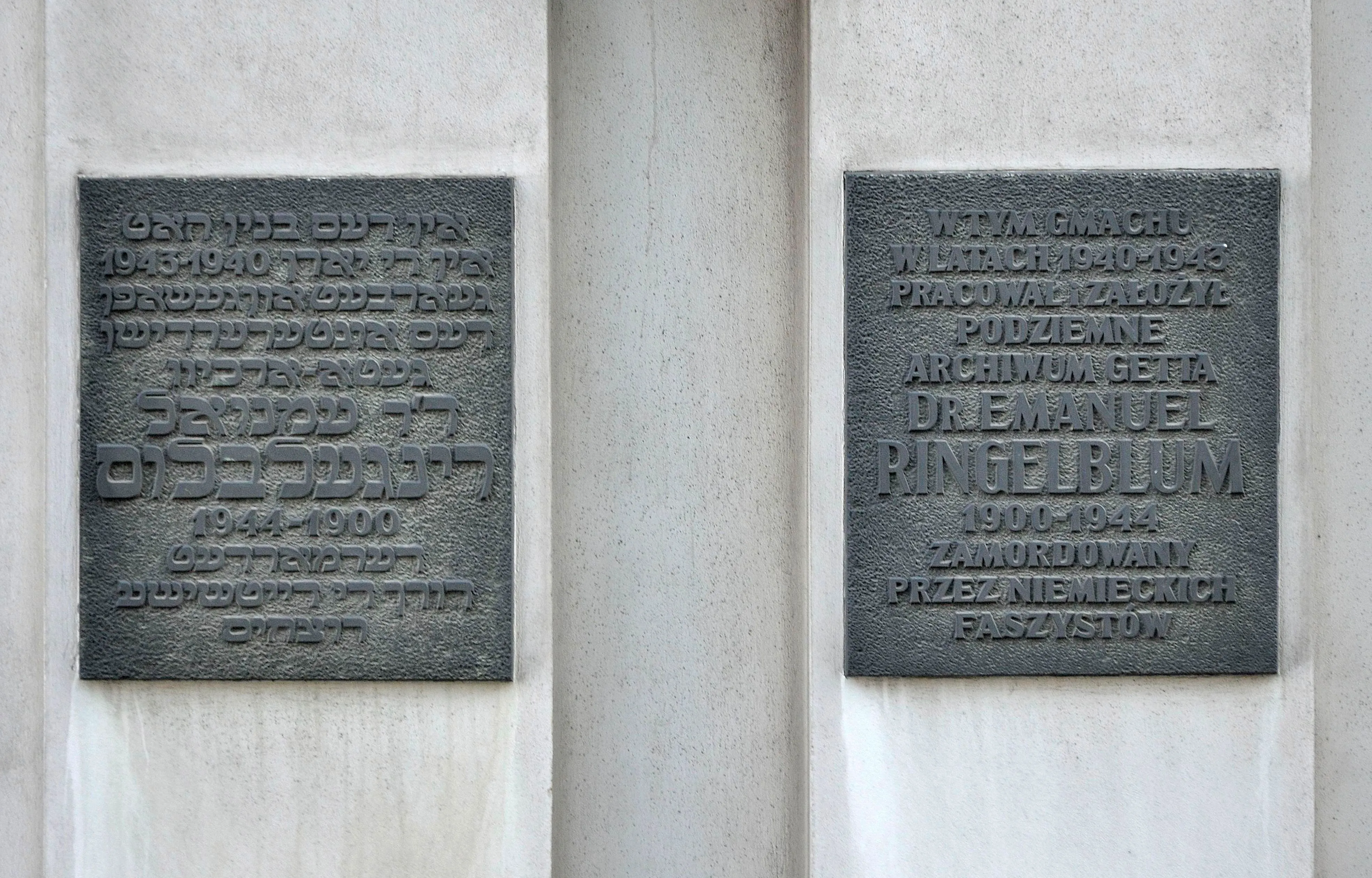 Twee donkere metalen plaquettes met inscripties in het Pools en Hebreeuws gemonteerd op een lichte muur