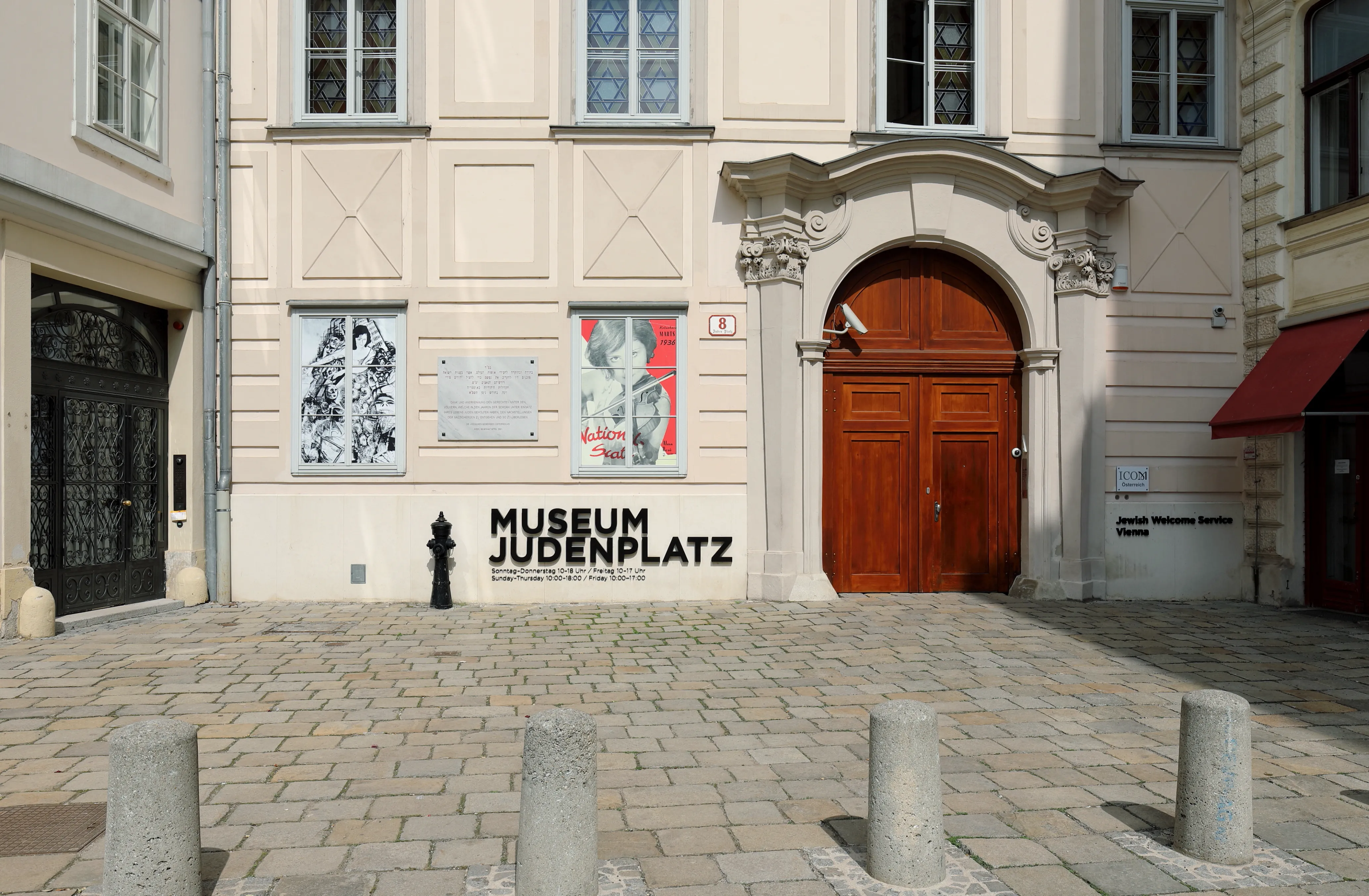 De buitenkant van het Joods Museum Wenen op de Judenplatz, met een wit gebouw met een houten deur en een bord aan de muur.