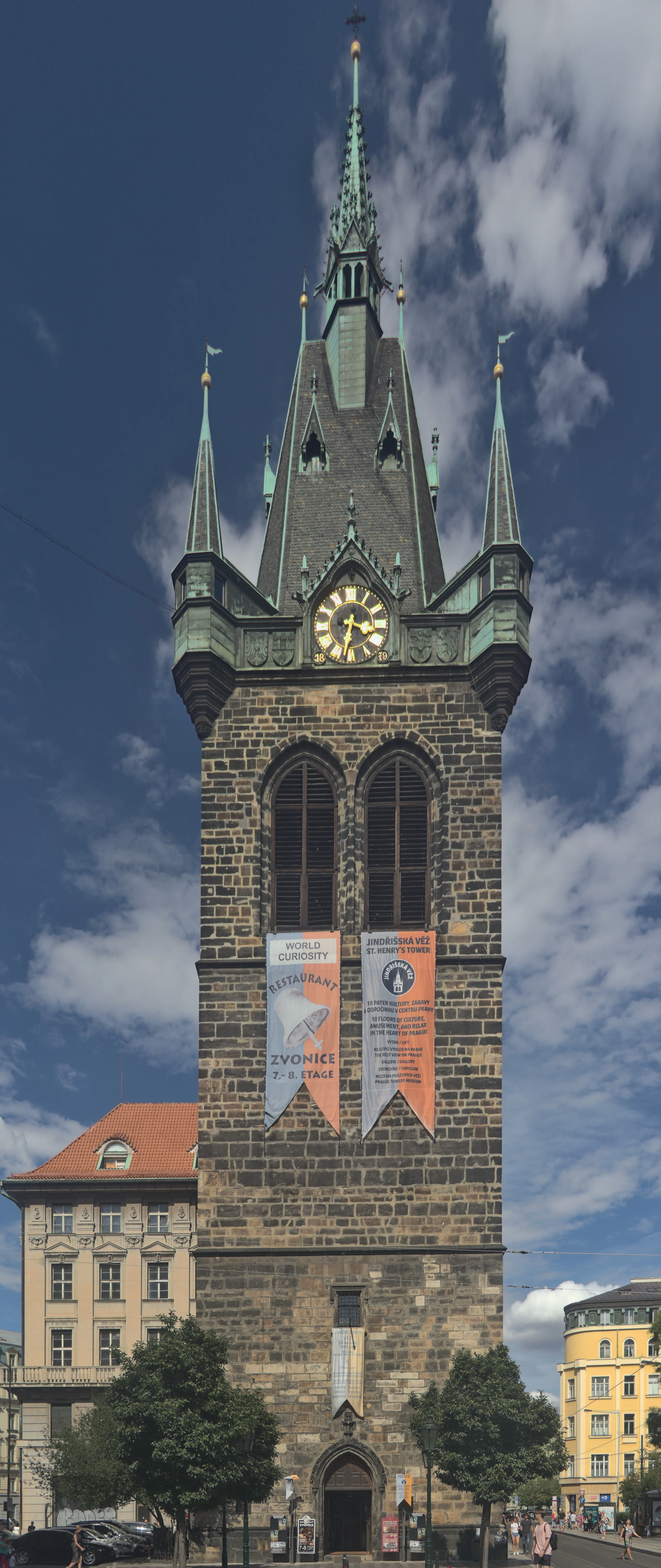Hoge stenen toren met een klok en groene spitsen onder een blauwe hemel