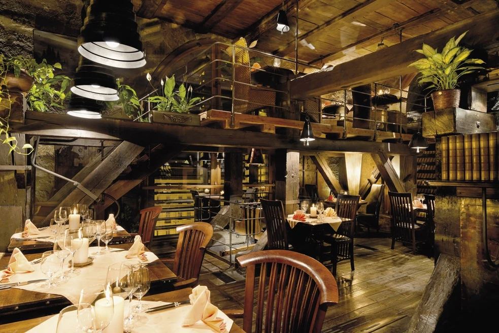mesas de madera puestas para comer en un interior rústico con vigas expuestas y paredes de piedra