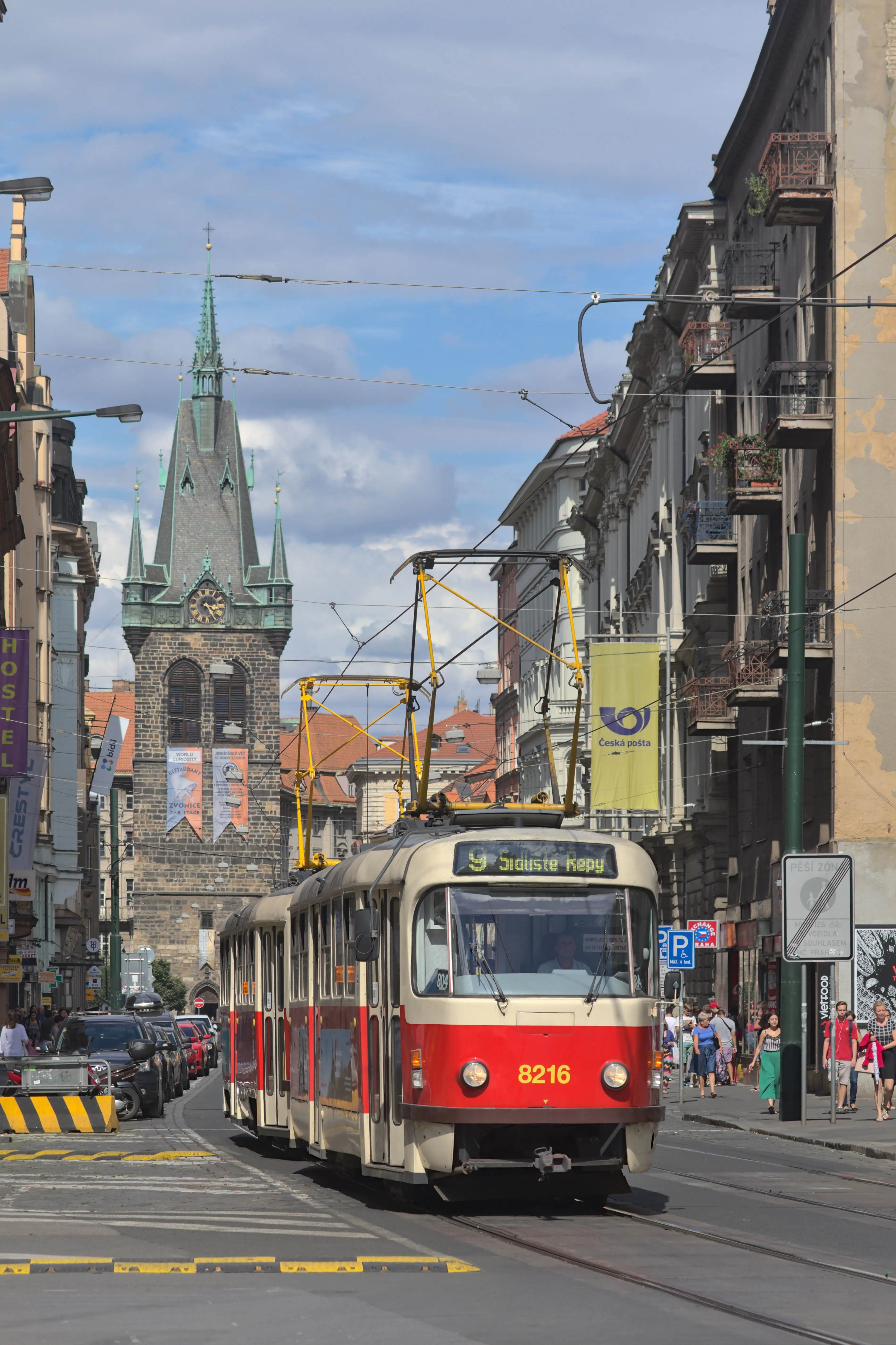 Een rode en crèmekleurige tram op rails met de Jindřišská Toren op de achtergrond