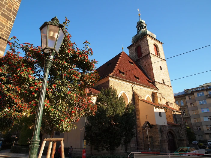 Jindřišská Toren met een groen gedekte spits naast een kerk, een straatlantaarn en een boom met rode bessen onder een blauwe hemel