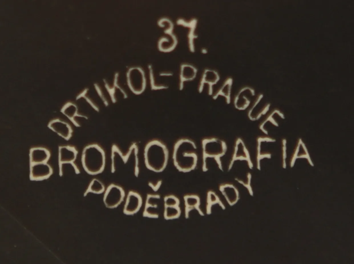 zbliżenie zabytkowego stempla do odbitek fotograficznych z tekstem '37. ORTIKOL-PRAGUE BROMOGRAFIA PODĚBRADY' ułożonym w okrąg