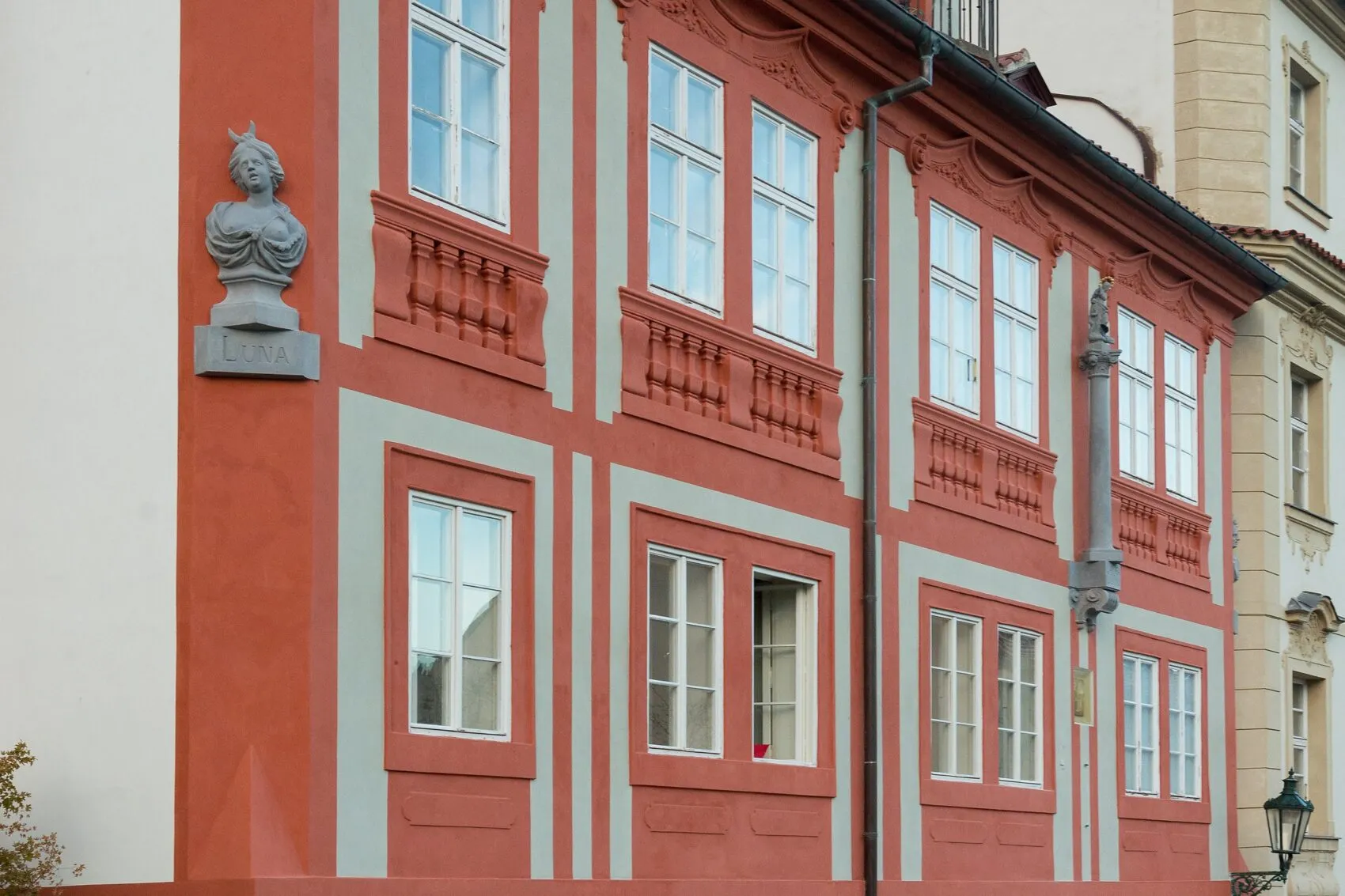 Czerwony budynek z białymi zdobieniami i popiersiem Josefa Sudka na fasadzie