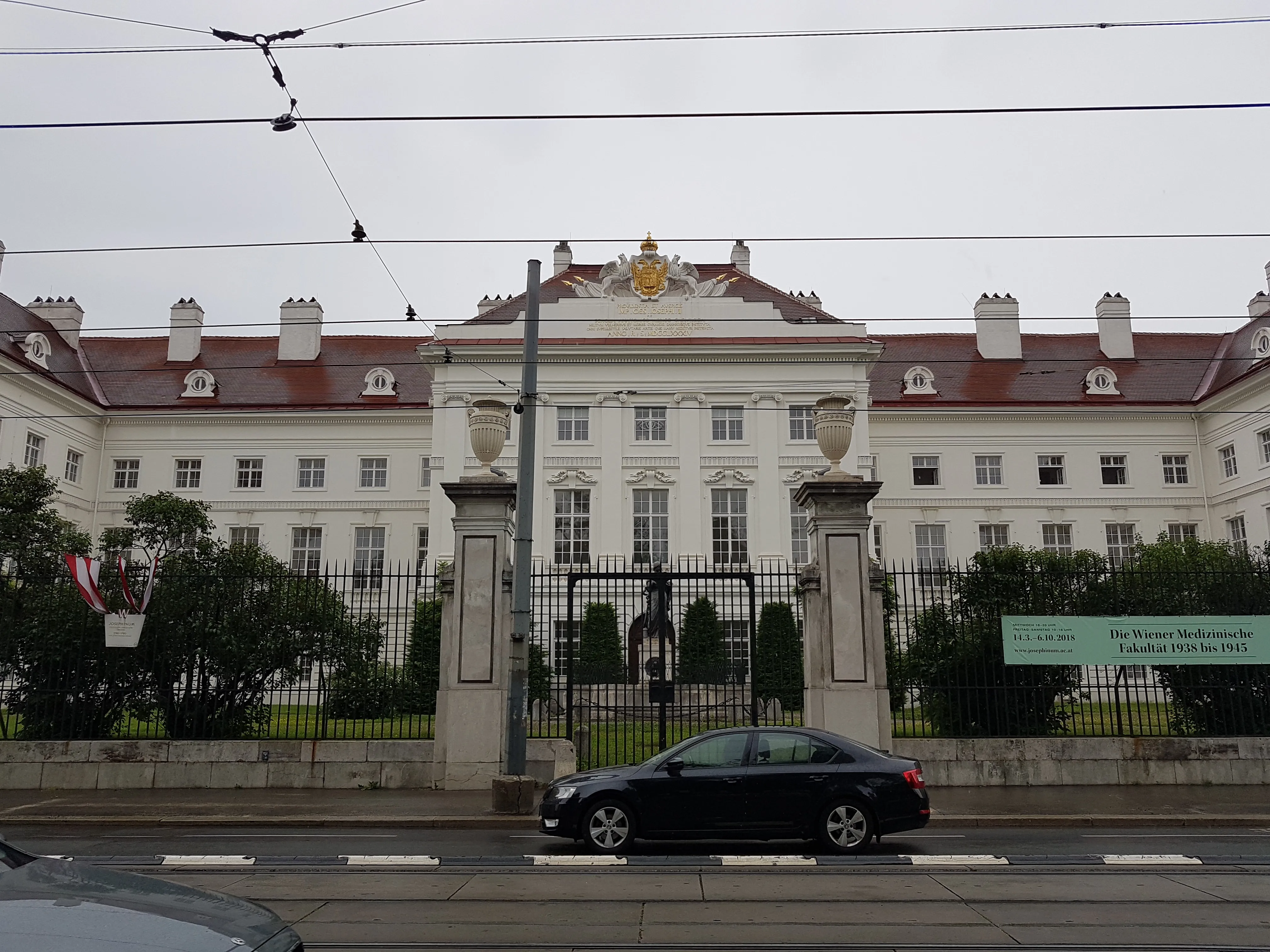 White classical building with red roof and black gate, cars on the street in front