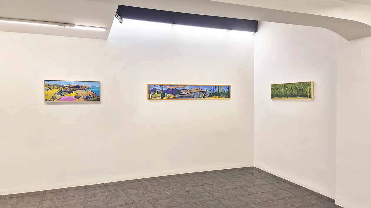 Three colorful landscape paintings hanging on white walls in a gallery corner with overhead track lighting.