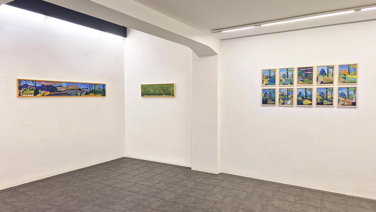 White-walled gallery room with framed landscape paintings displayed on the walls under track lighting, with gray carpeted floor