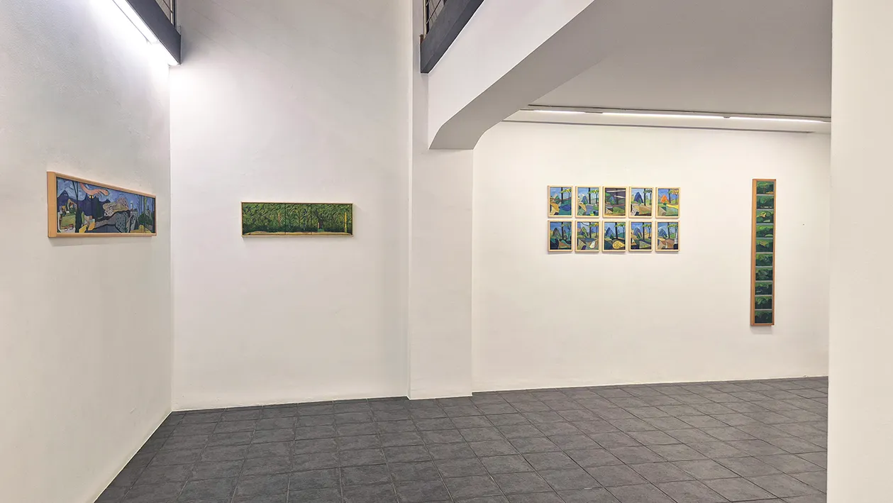 White gallery walls displaying several framed paintings, including a grid of nine small landscapes and a tall vertical piece, under track lighting.