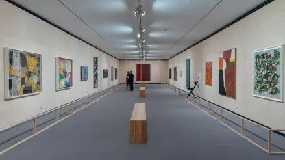 długa galeria-hol z nowoczesnymi dziełami sztuki na białych ścianach i drewnianymi ławkami