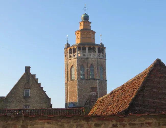 Histórico campanario de ladrillo con cúpula de cobre verde que se alza sobre los tradicionales tejados de hastiales escalonados contra un cielo azul despejado