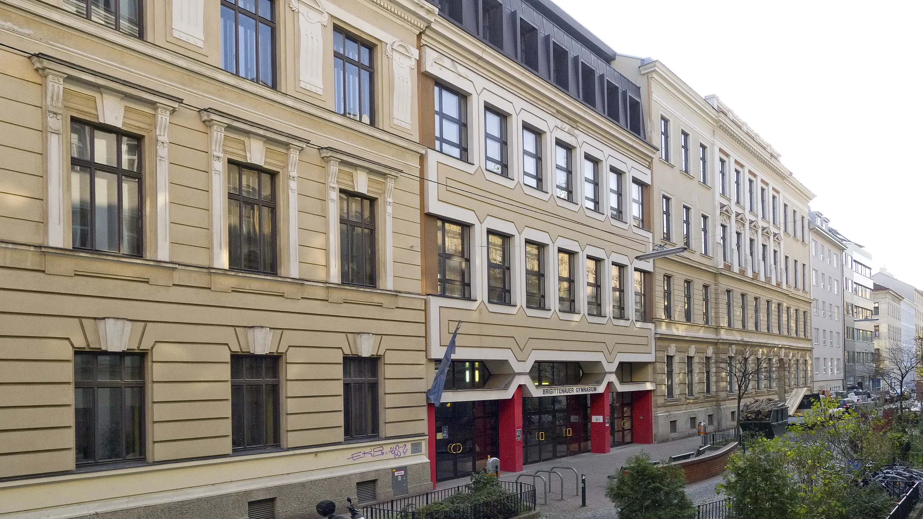 Beige building with multiple windows and a modern entrance with red accents and a blue flag