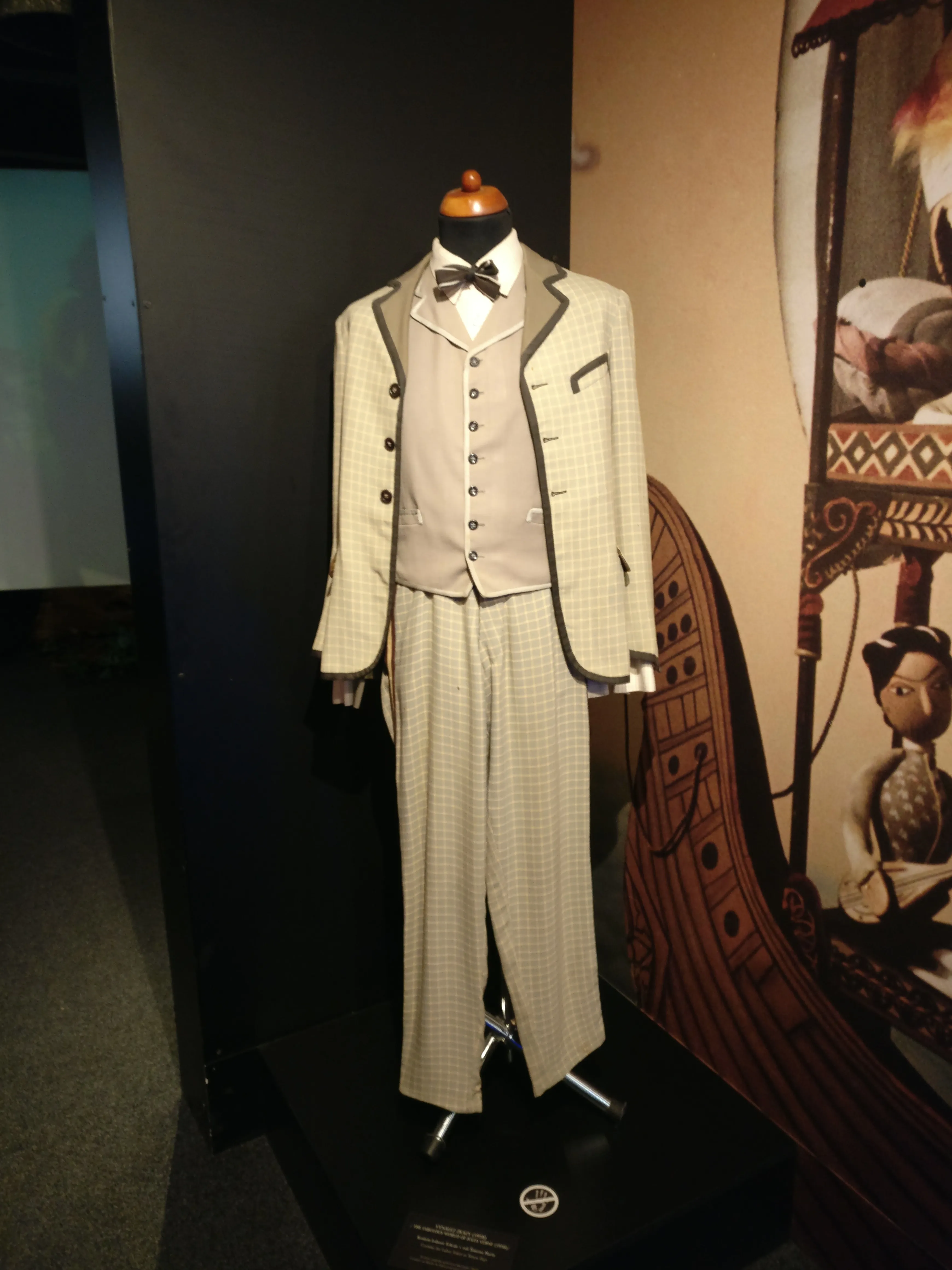 A mannequin wearing a light-colored checkered suit with a vest and bow tie, displayed in a museum exhibit.