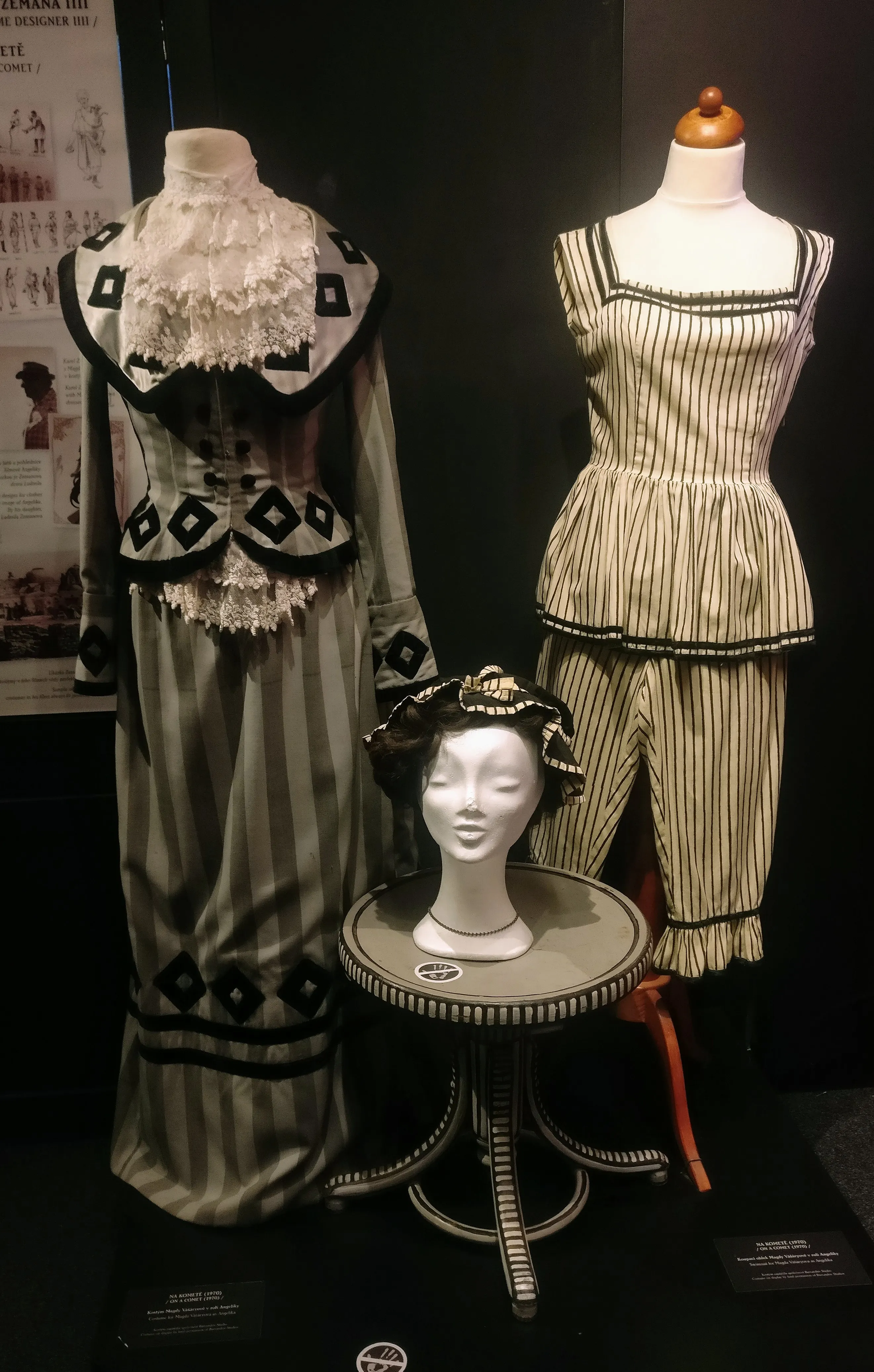 Two costumes on mannequins and a head mannequin on a table, featuring striped patterns and decorative elements