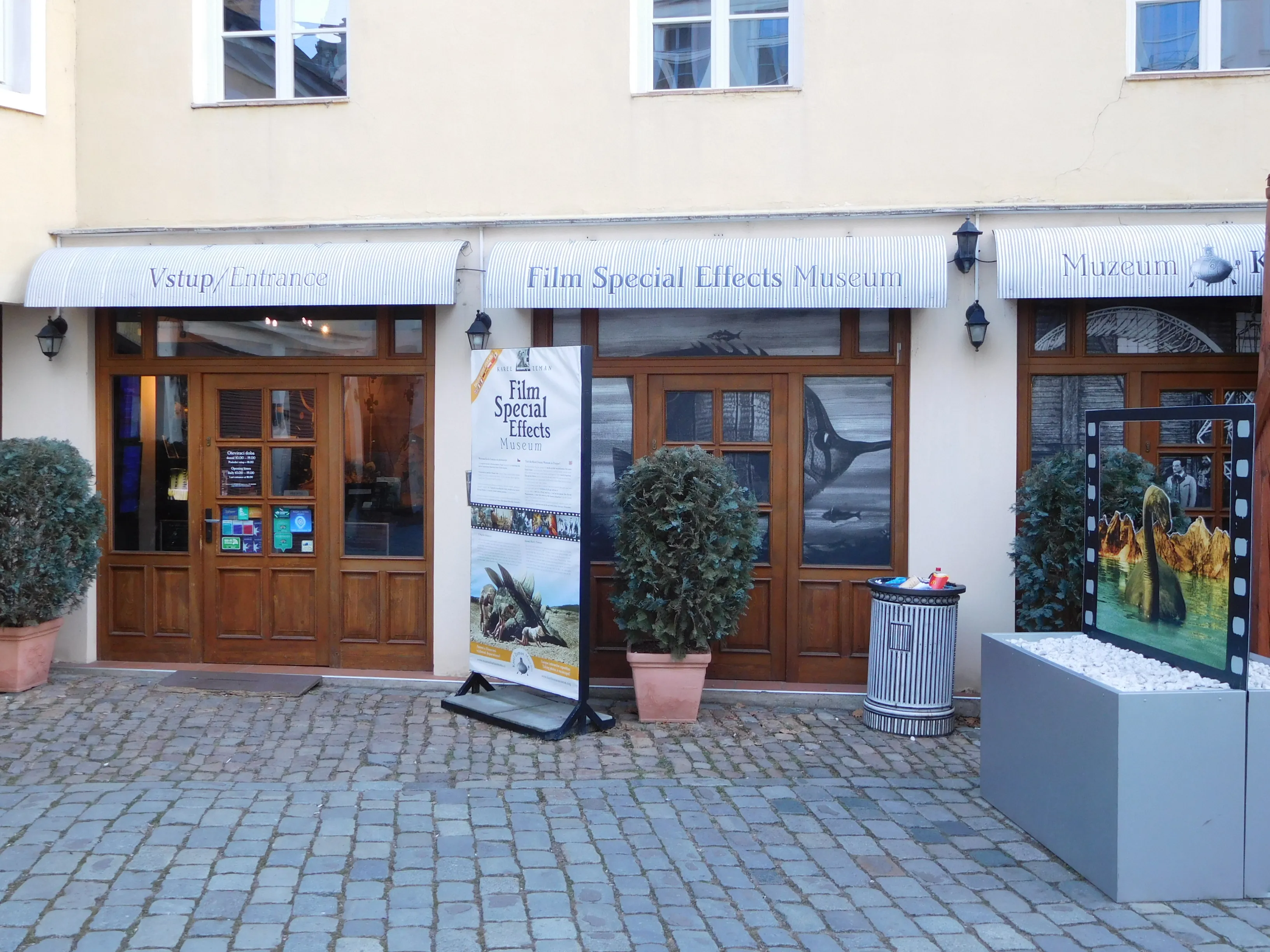 Exterior of the Karel Zeman Museum with wooden doors, a sign for Film Special Effects Museum, and potted plants on a cobblestone pavement