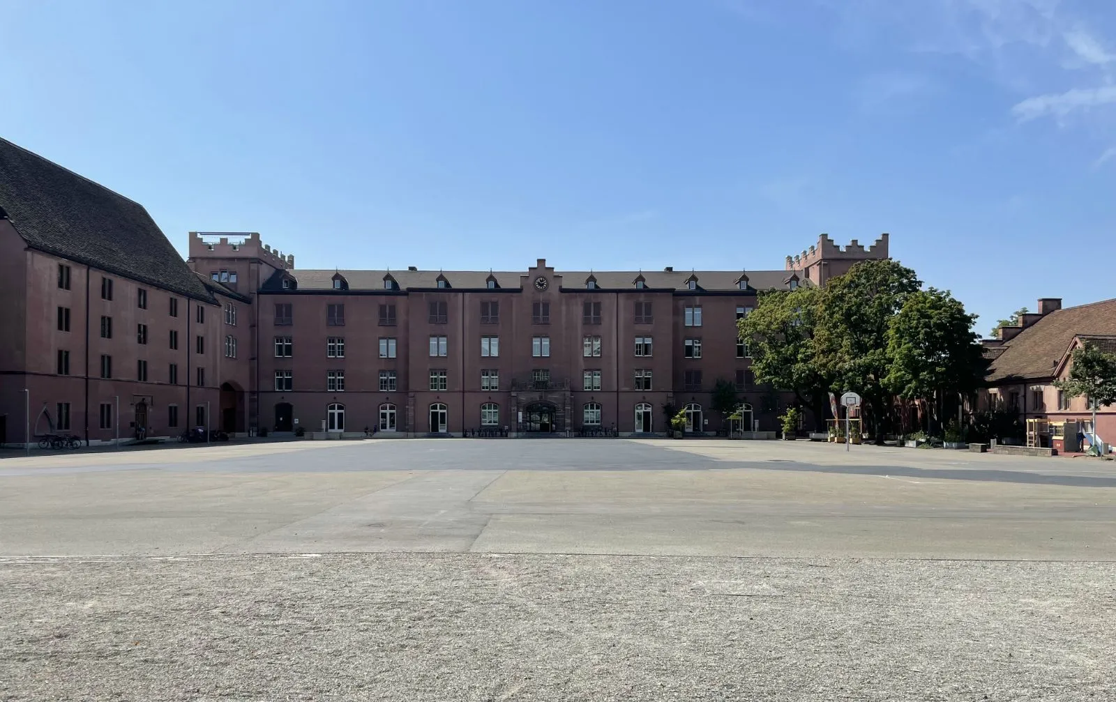 Edificio de cuartel de ladrillo rojo con torres y hastiales escalonados que rodea un amplio patio empedrado bajo un cielo azul despejado