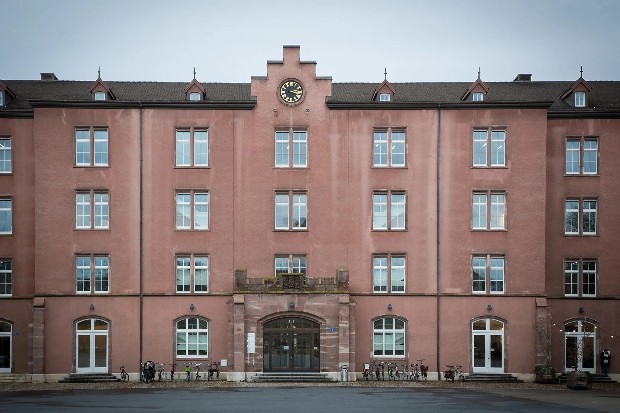 Fachada rosa de Kaserne Basel con ventanas simétricas, reloj central y entrada arqueada