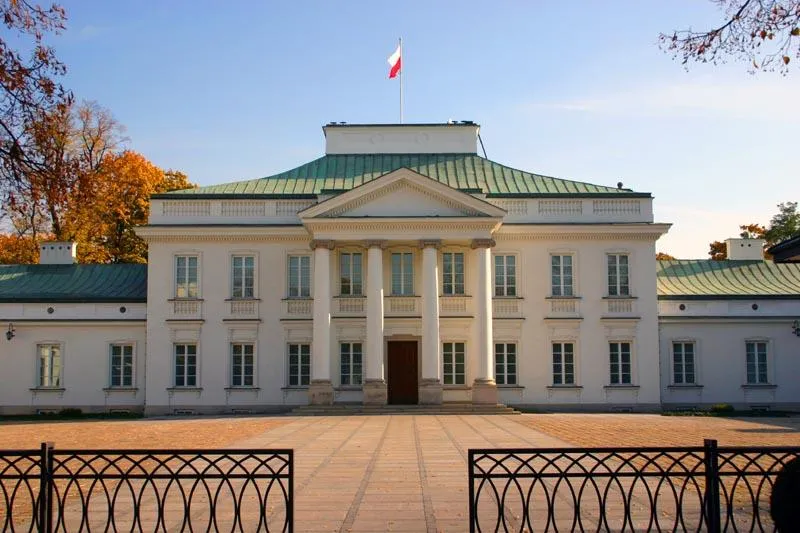 Budynek neoklasycystyczny z białym frontem, zielonym dachem i polską flagą na szczycie