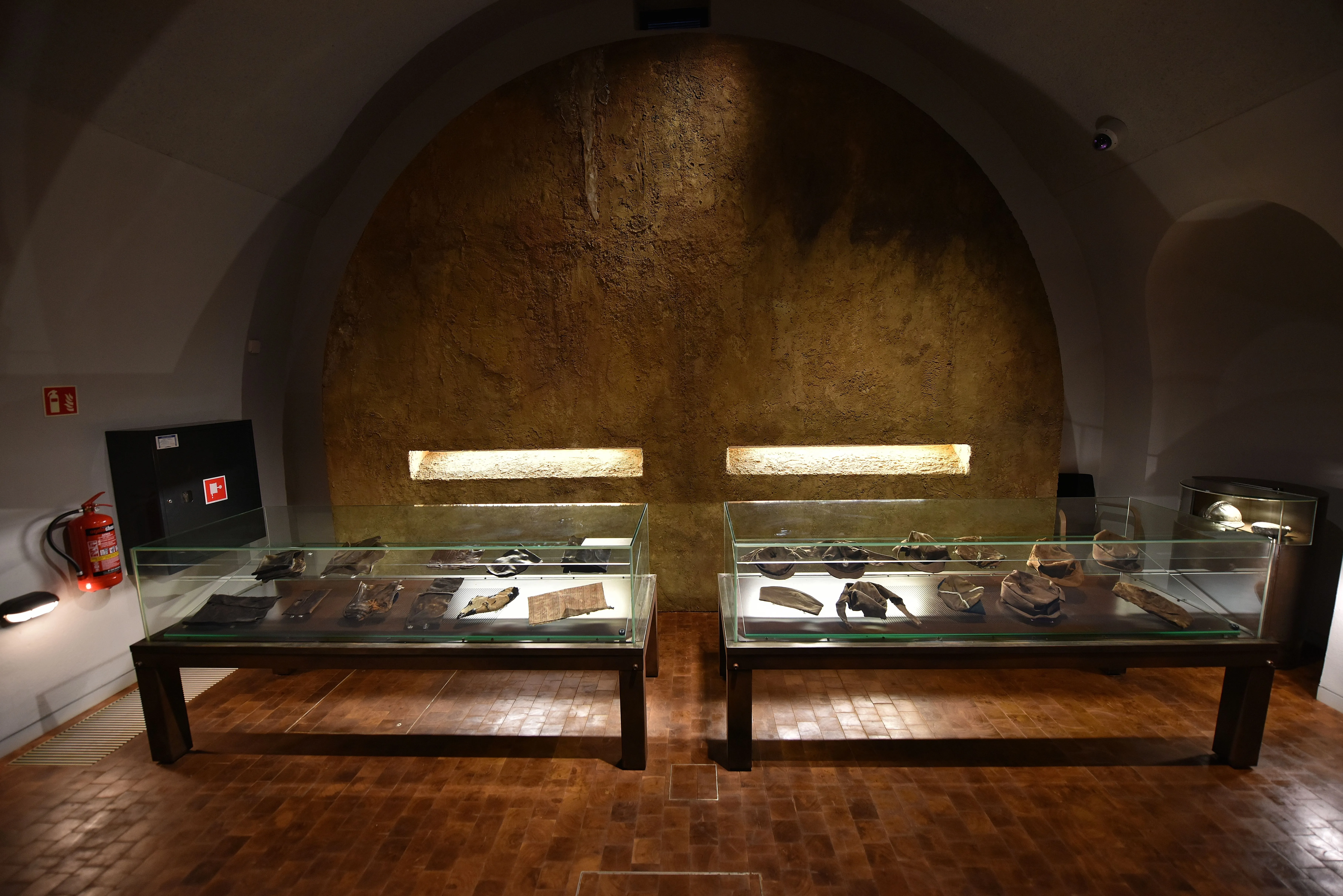 Glazen vitrines met artefacten onder warme verlichting in een museuminterieur met een boogmuur