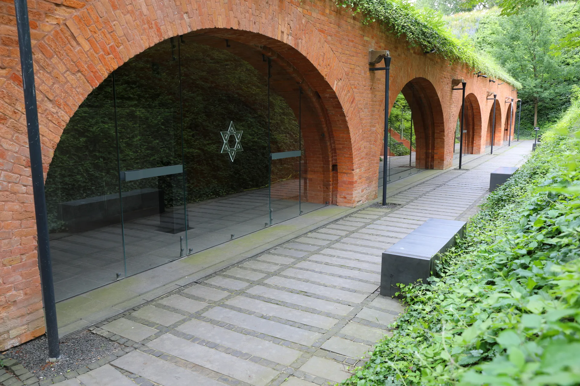 Rode bakstenen bogen met glazen deuren bij het Katyń Museum, omringd door groen en een verharde wandelweg